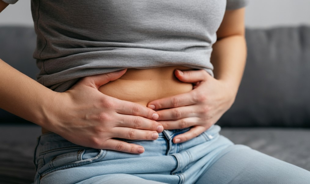 Girl holding her muffin tops with hands, while seating on sofa